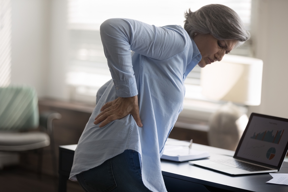 Rear side view aged woman stand near workplace desk