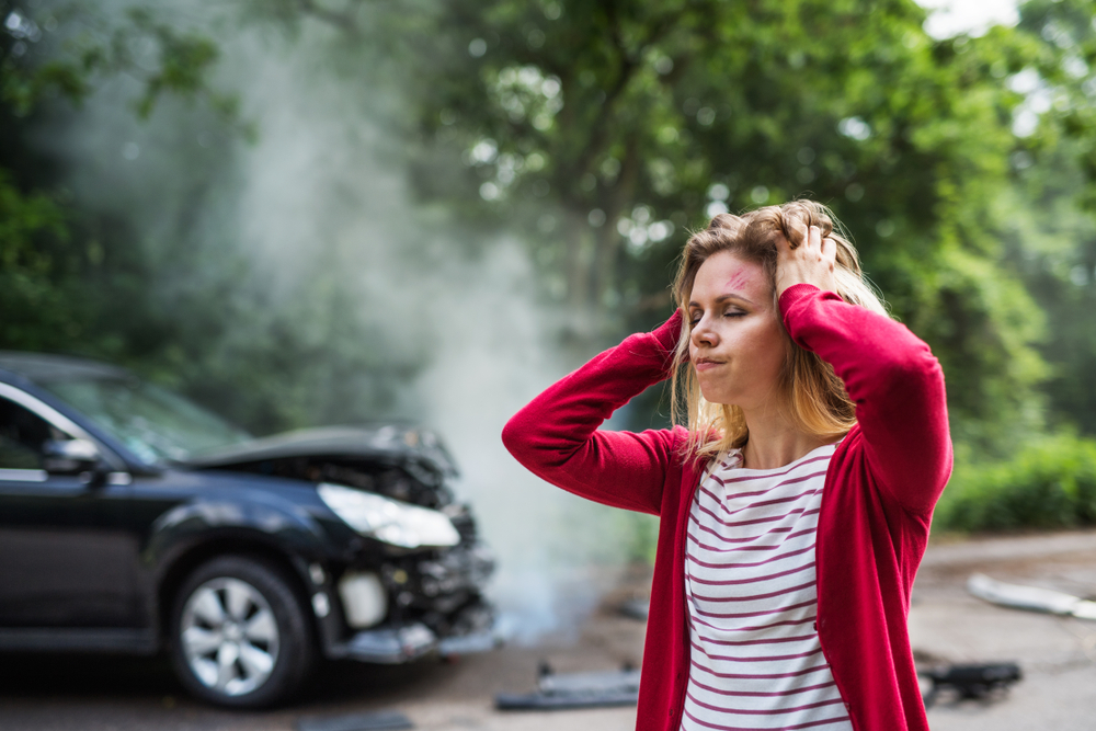 An injured young woman standing by the damaged car after a car accident