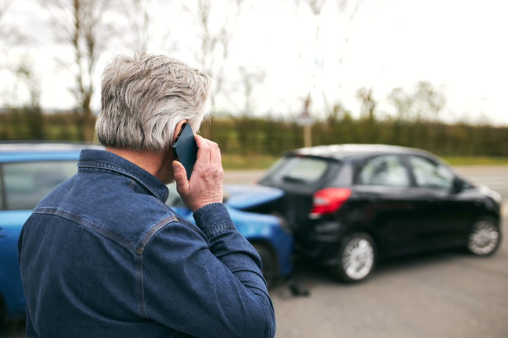Rear view of senior male driver standing by damaged car after traffic accident